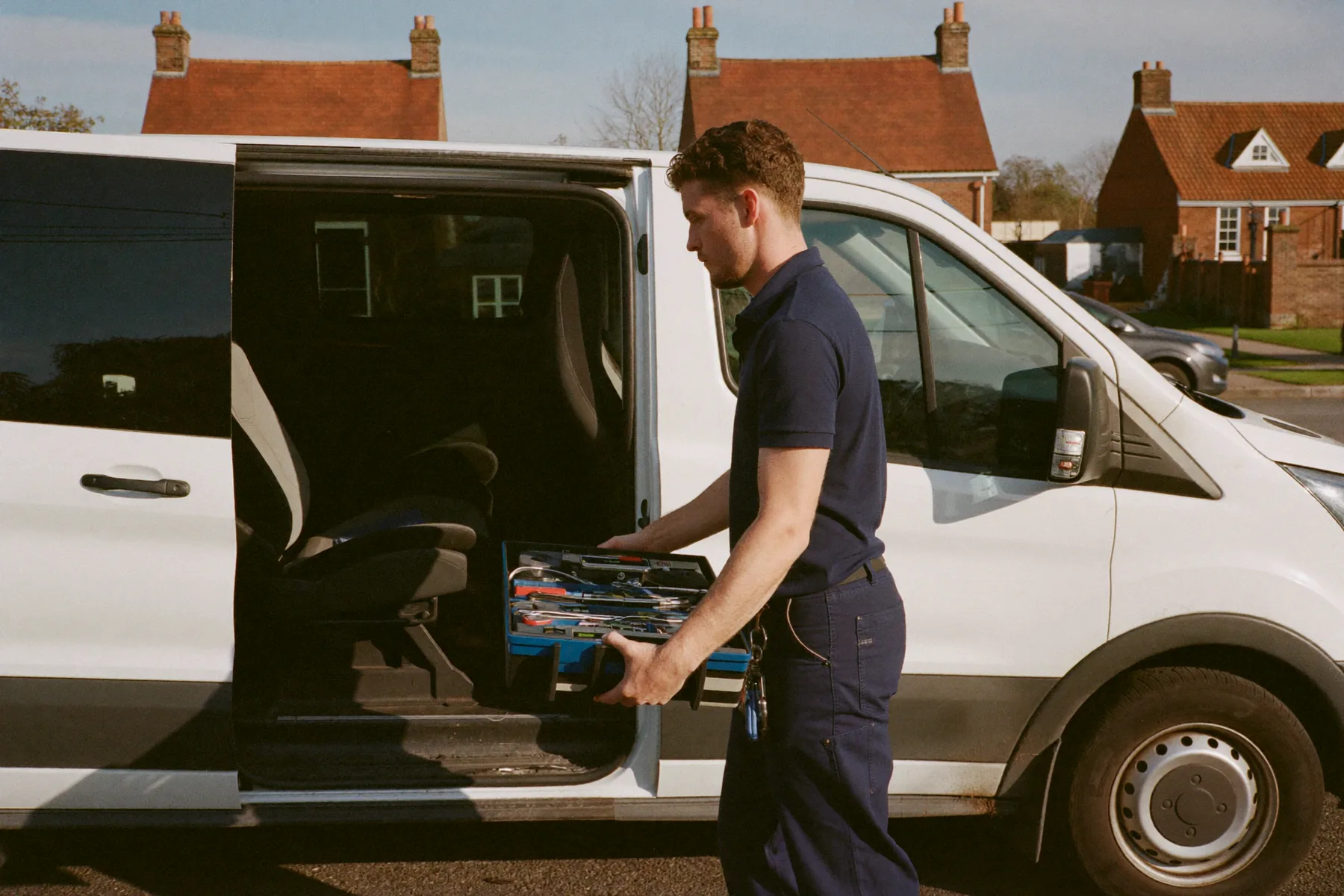 A South East Plumbing engineer lifting a tool tray out of the side door of a work van on a suburban Kent street.