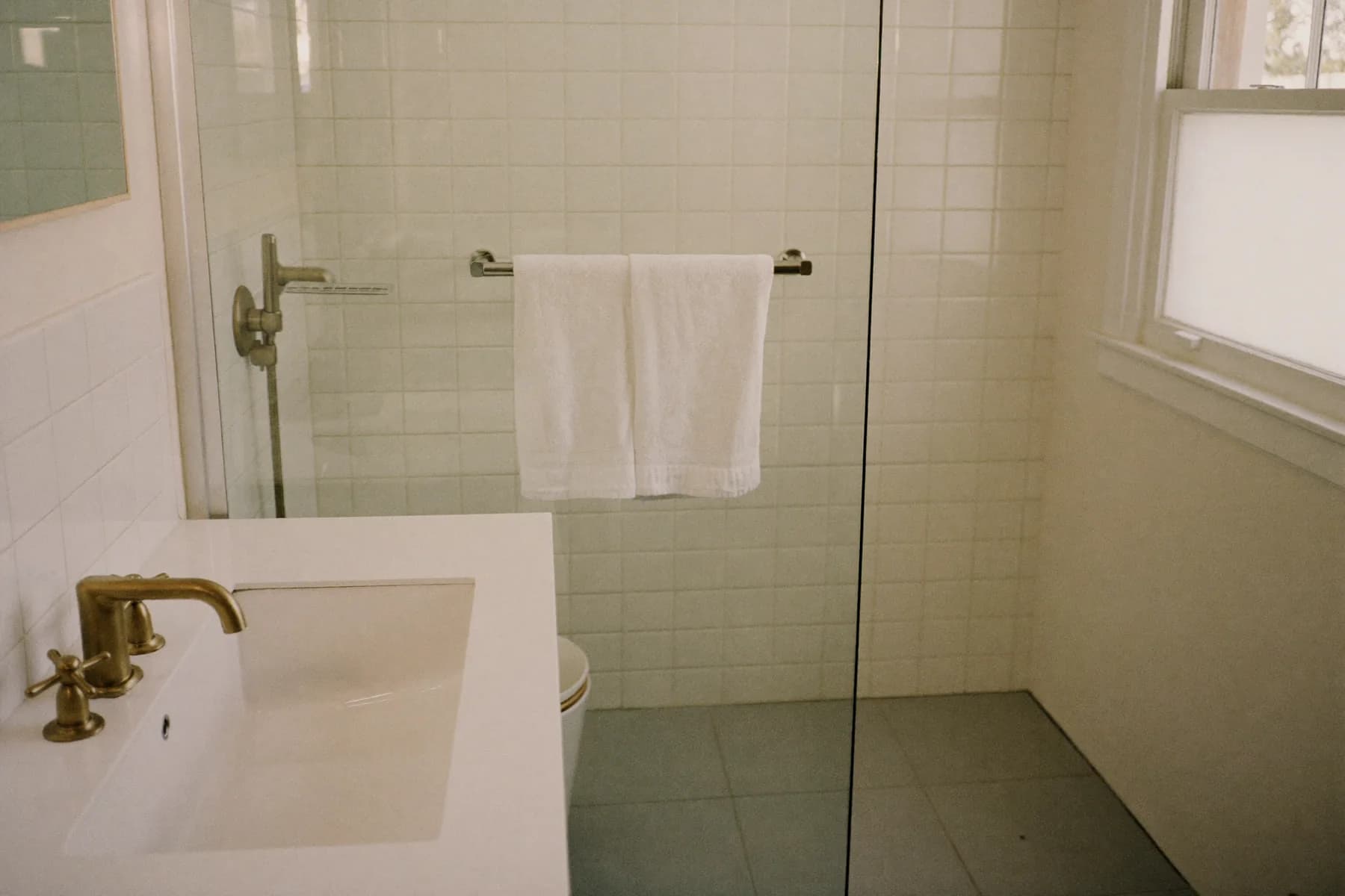 A newly finished bathroom in an ordinary British home with white metro tiles, a brushed brass tap and a simple white basin.