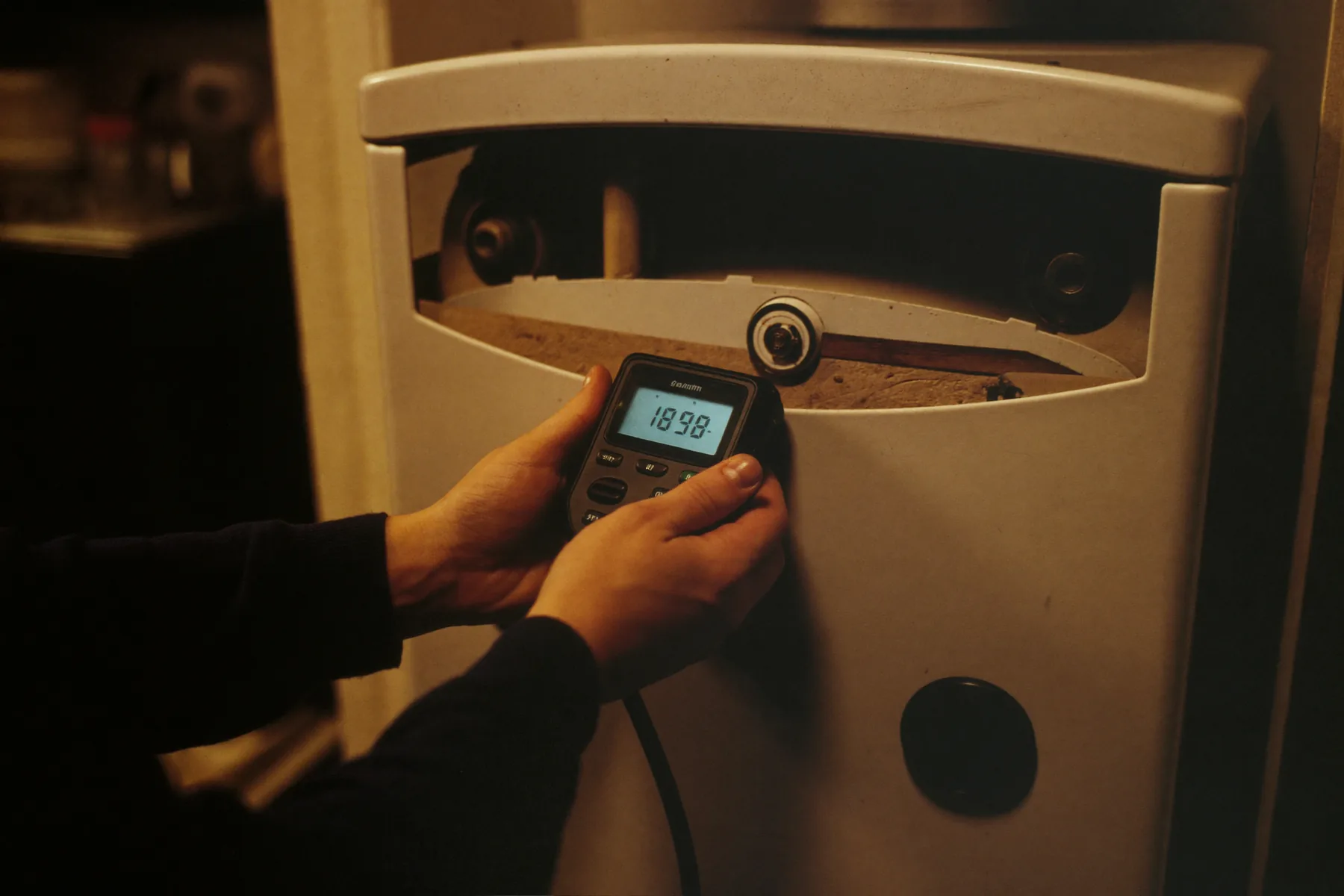 A gas engineer holding a digital manometer against a boiler test point, with the boiler casing removed.